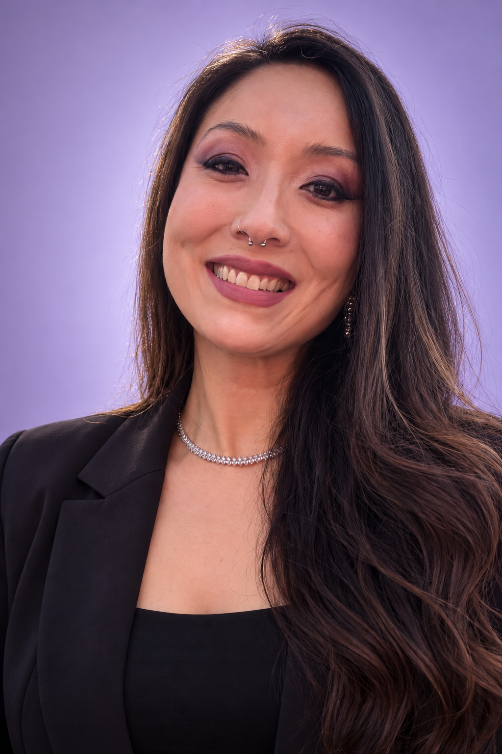 Denise Lumie Fujita, de blazer preto, em retrato com fundo lavanda